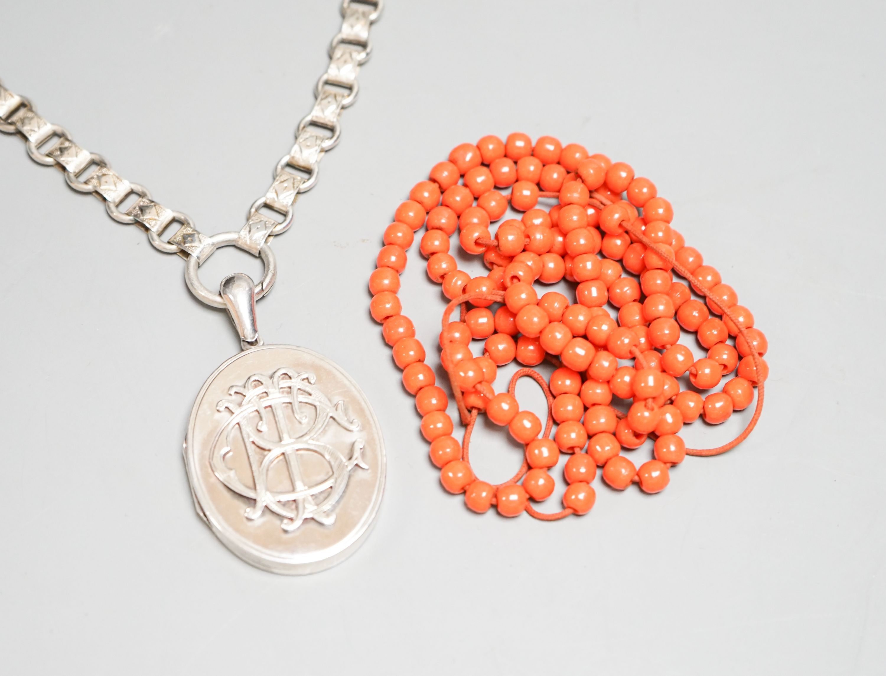 A white metal oval locket with monogram, 43mm, on a fancy white metal chain and a string of coral coloured glass beads.